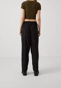 Černé tepláky s bílými linkovými vzory a elastickým pasem, doplněné o úzký olivově zelený crop top. Hladká textilie.