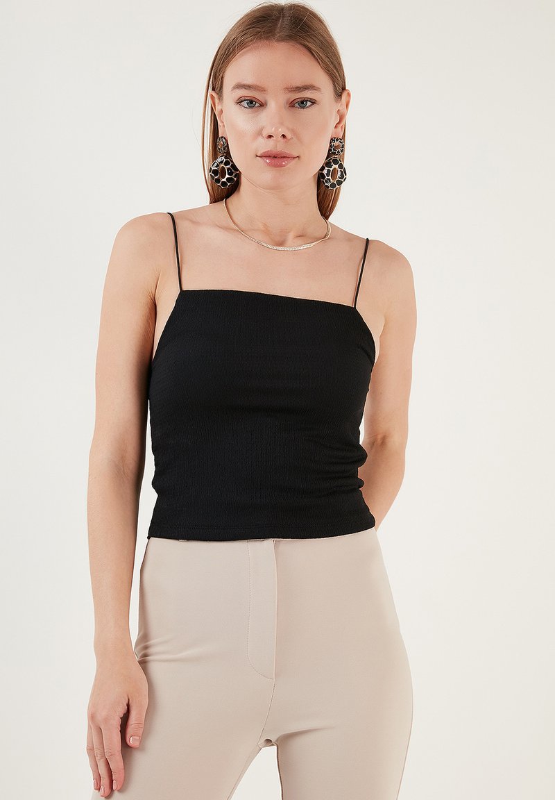 Top aderente nero con spalline sottili e tessuto testurizzato, abbinato a pantaloni beige a vita alta. Scollatura semplice e design aderente.
