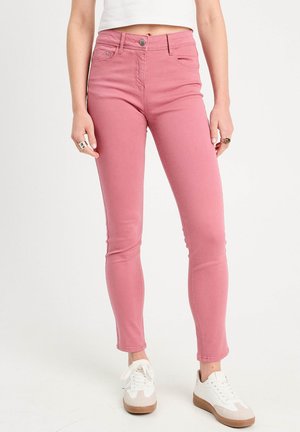 Jean skinny rose taille haute, avec fermeture à boutons sur le devant, quatre poches et texture en denim lisse. Associé à des baskets blanches.