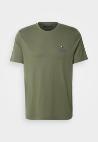 Camiseta de algodón verde oliva con cuello redondo, mangas cortas y un pequeño logo bordado en el pecho izquierdo. Textura lisa, corte holgado.