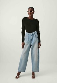 Top preto de manga longa combinado com jeans de perna larga azul clara. Os jeans possuem uma cintura alta e bolsos frontais, com uma textura de denim suave.