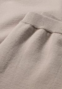 Beiger Strickstoff mit Rippbund-Textur. Glatte, weiche Oberfläche mit subtilen Farb- und Webmuster-Variationen.