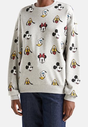 Harmaa collegepaita, jossa toistuvia sarjakuvahahmoja Mickey Mousesta, Minnie Mousesta, Aku Ankasta ja Plutosta, käytetty tummansinisten farkkujen kanssa.