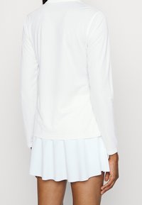 Långärmad vit topp med en slät textur, tillsammans med en ljusblå utsvängd kjol. Båda plaggen har en enkel och ren design.