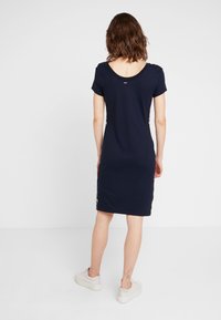 Marinblå klänning med kort ärm och rundad rygg. Har en figursydd design och kontrasterande sidodelar. Tyget ser mjukt och slätt ut.