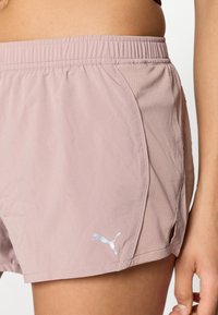 Ανοιχτό ροζ αθλητικό σορτς με ελαστική μέση και πλευρικό άνοιγμα. Διαθέτει αντανακλαστικό λευκό λογότυπο Puma στο κάτω μέρος αριστερά.