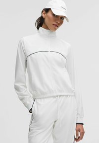 Valge tõmbluku ees oleva jakk, millel on sobiv talje, musta ääre kaunistustega ja pikad varrukad. Koos sobivate valgete pükstega ja mütsiga.