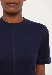 Marineblaue T-Shirt mit Rundhalsausschnitt, kurzen Ärmeln und einer mittigen Naht, die mit kontrastierendem orangefarbenem Stitching versehen ist. Aus glattem Baumwollmaterial.