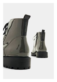 Bottes courtes gris foncé brillantes avec semelles épaisses noires et languettes à l'arrière, une botte au premier plan et une floue en arrière-plan.