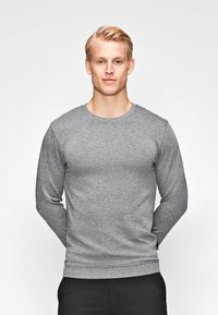 Grauer Sweatshirt mit langen Ärmeln und Rundhalsausschnitt aus strukturiertem Stoff, körperbetonter Schnitt und Rippbündchen, kombiniert mit schwarzen Hosen.