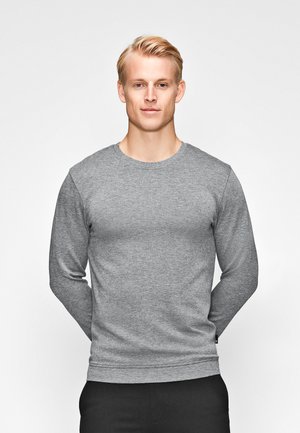 Grauer Sweatshirt mit langen Ärmeln und Rundhalsausschnitt aus strukturiertem Stoff, körperbetonter Schnitt und Rippbündchen, kombiniert mit schwarzen Hosen.