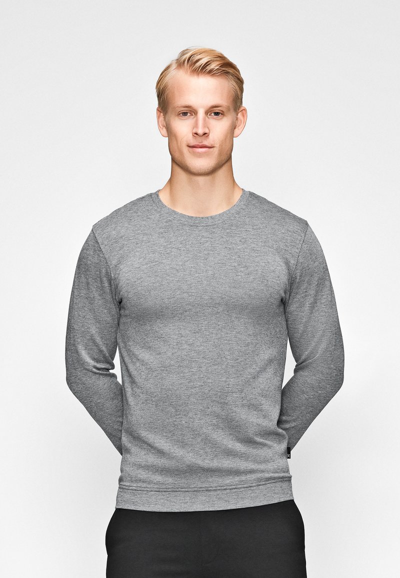 Grauer Sweatshirt mit langen Ärmeln und Rundhalsausschnitt aus strukturiertem Stoff, körperbetonter Schnitt und Rippbündchen, kombiniert mit schwarzen Hosen.