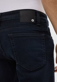 Jeans in denim blu scuro con una toppa in pelle nera in vita con dettagli del logo, tasche posteriori cucite e design classico a cinque tasche.