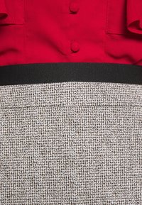 Punainen yläosa, jossa on pyöreät napit ja rypistetyt hihat, yhdistettynä teksturoituun musta-valkoiseen kuosiskirtkiin, jossa on musta vyötärönauha.