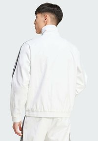 Vit zip-up jacka med hög krage, elastiska ärmslut och svarta sidostråk. Lättviktig tyg med en slät textur och avslappnad passform.