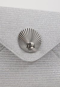 Srebrna kopertówka o teksturowanej powierzchni, z zapięciem w kształcie wachlarza i klapą na zakładkę.