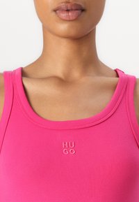 Rosa gerippter Tanktop mit rundem Ausschnitt und gesticktem "HUGO"-Logo in passender Farbe. Glatte Textur mit breiten Trägern.