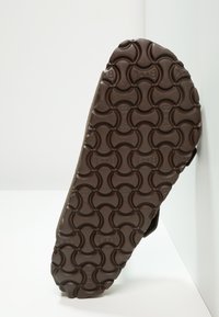 Brown rubber shoe sole with a circular textured pattern and embossed brand logos, showing a durable, non-slip design.