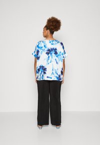 Korte ermest bluse i hvit med blå blomsterprint, kombinert med svarte folder vide bukser og blå hæler.