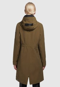 Olivgrön parka med huva, som har en åtsittande midja, långa ärmar och en delad nederkant. Logotypen är synlig på baksidan av kragen.