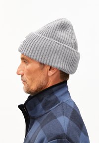 Grijze gebreide beanie met ribbeltextuur en omgeslagen rand, gedragen door een man in een blauw geruite fleecejas.