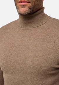 Brauner, gerippter Rollkragenpullover aus weichem, strukturiertem Stoff. Der Kragen ist eng anliegend und die gesamte Passform ist körpernah.