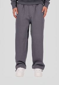 Szare spodnie dresowe o luźnym kroju, z elastycznym pasem i zamkami na mankietach u dołu nogawek, zestawione z białymi trampkami na neutralnym tle.