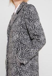 Szary płaszcz w wzór lamparta, wykonany z miękkiego materiału. Posiada klapy i boczne kieszenie dla dodatkowej wygody.