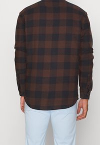 Camisa de manga larga a cuadros marrones y azul marino con botones en los puños, hecha de una tela texturizada, con un dobladillo curvado.
