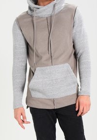 Pullover con cappuccio realizzato in un mix di tessuti grigio chiaro e taupe, con maniche grigie testurizzate e tasca frontale. Design casual e aderente.