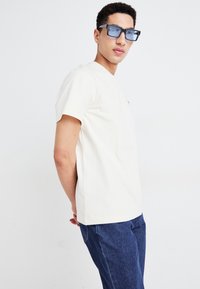 Witte korte mouwen t-shirt met een ronde hals, gecombineerd met blauwe denim jeans en oversized vierkante zwarte zonnebril.