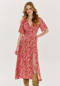 Květinové midi šaty v růžových a žlutých odstínech, s krátkými rukávy, hlubokým výstřihem do V a bočním rozparkem. Kombinované s koženými kozačkami do kolen v béžové barvě.