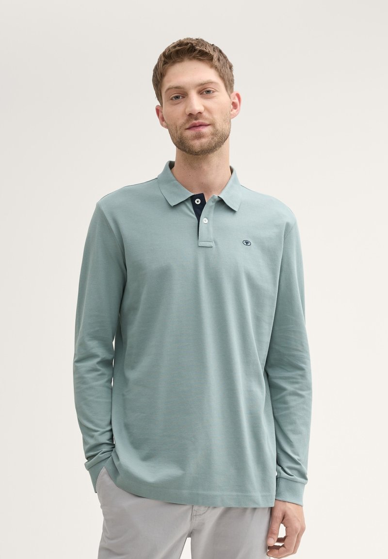 Langærmet polo shirt i lyseblå med en marineblå krave. Har et lille logo på brystet og en glat bomuldsstruktur.