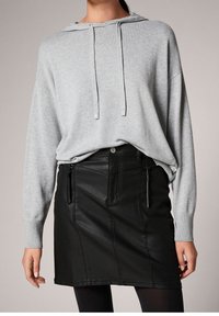 Hoodie harmaa vaaleasta päältä, jossa on etupuolella kenguru-tasku ja nyörit, yhdistetty mustaan nahkaiseksi minihelmaksi, jossa on sivuvetoketjuyksityiskohtia.