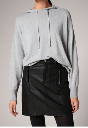Un sweat à capuche gris clair avec une poche kangourou à l'avant et des cordons de serrage, associé à une mini-jupe en cuir noir avec des détails de zip sur les côtés.