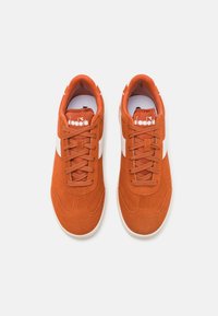 Oransje semskede sneakers med hvite detaljer, som har en teksturert overflate, rund tå og tradisjonelt snøring.