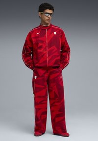 Rode sportjack en broek set met een geometrisch patroon, voorzien van witte accenten en het Puma-logo, gemaakt van lichtgewicht stof.