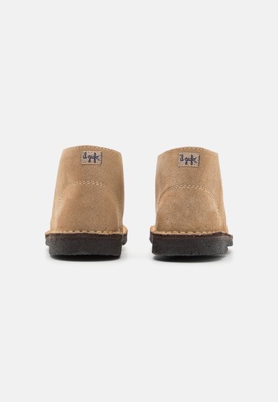Cizme de gleznă din suede bej cu un designrotund, talpă din cauciuc maro închis contrastant și detalii din piele cusute la călcâi.