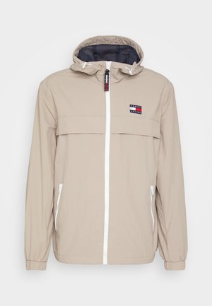 Jasno beżowa kurtka z kapturem, białym zamkiem błyskawicznym z przodu, zapinanymi na zamek bocznymi kieszeniami, elastycznymi mankietami oraz małym logo Tommy Jeans na piersi.