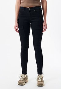 Black cargo jeans with a slim fit, featuring side pockets and a button closure. Paired with beige sneakers for contrast.