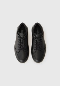 Black leather sneakers with rounded toe, textured body, smooth accents, and flat laces. Features contrast stitching and cushioned insole.