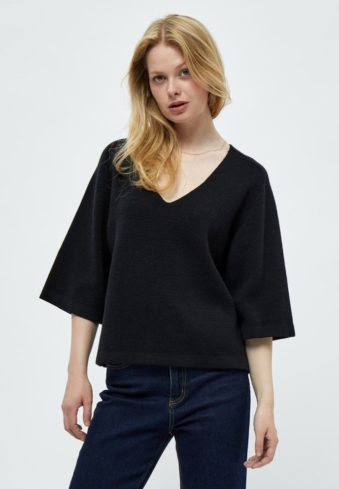 Pullover nero a V con maniche larghe, realizzato in un materiale a maglia testurizzato. Indossato con jeans scuri, presenta una vestibilità ampia e rilassata.
