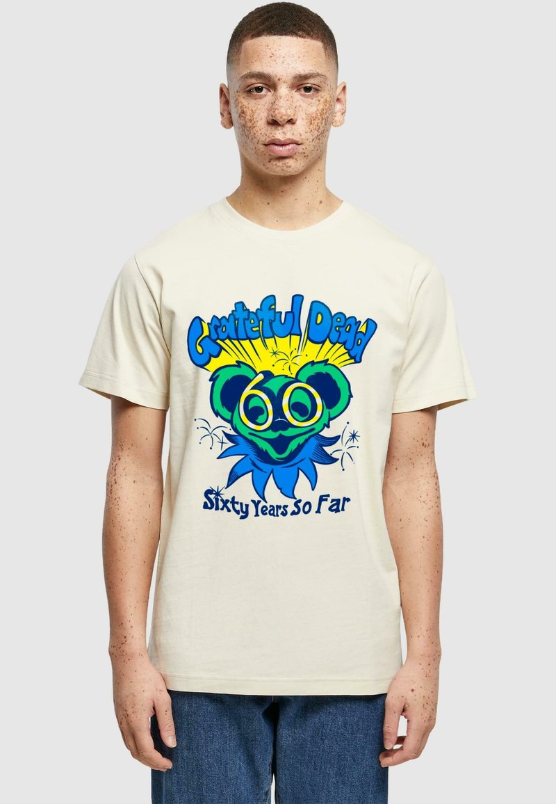 T-shirt en coton crème avec une impression graphique vibrante. Le design présente un ours aux grands yeux et accents bleus, le texte indique "Grateful Dead Sixty Years So Far".