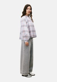 Gecontroleerde oversized blouse in lichte stof met puffmouwen, gecombineerd met high-waisted, loszittende grijze spijkerbroeken en zilveren schoenen.