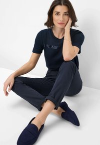 Marine T-shirt met een sequined streep, gecombineerd met slim-fit marinebroeken en marine instappers. Zachte stof textuur, casual pasvorm.