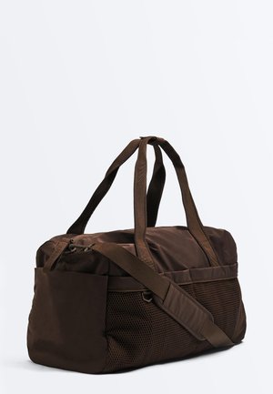 Brązowa sportowa torba typu duffel z podwójnymi uchwytami, regulowanym paskiem na ramię, siateczkowymi bocznymi kieszeniami oraz główną komorą zapinaną na zamek błyskawiczny na białym tle.