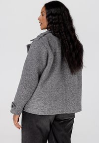 Grijze wolmix jas met een relaxte pasvorm, voorzien van een kraag, knoopmanchetten en een gestructureerde stof. Draag over een donkere broek.