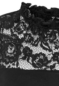 Černý krajkový top s květinovým vzorem a texturovaným designem, vybavený volánkovým výstřihem a hladkou látkou pod ním. Detailní krajkový překryv navrchu.