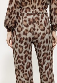 Leopardenmuster-Hosen aus weichem Stoff mit hoher Taille, in Brauntönen und Beige. Glatte Textur und fließendes Design sind sichtbar.