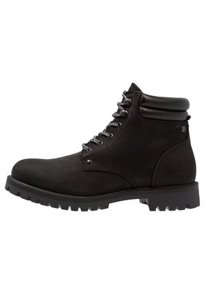 Botte de randonnée en cuir noir avec col rembourré à la cheville, œillets métalliques, semelle épaisse à crampons et fermeture à lacets sur le devant, vue de profil.